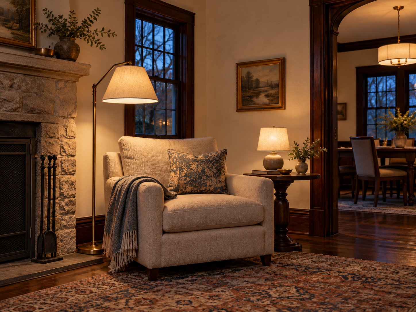 A reading chair lit by a floor lamp and table lamp beside a stone fireplace and dark wood arch.